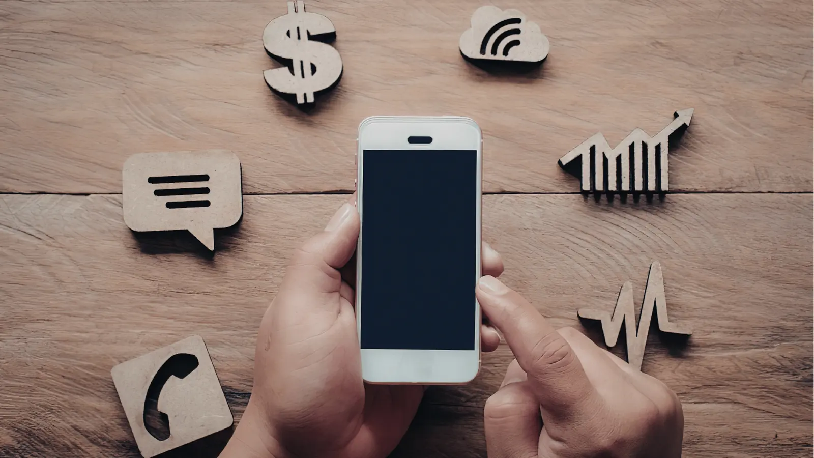 Hand holding smartphone over wooden table surrounded by wooden app icons for content calendar