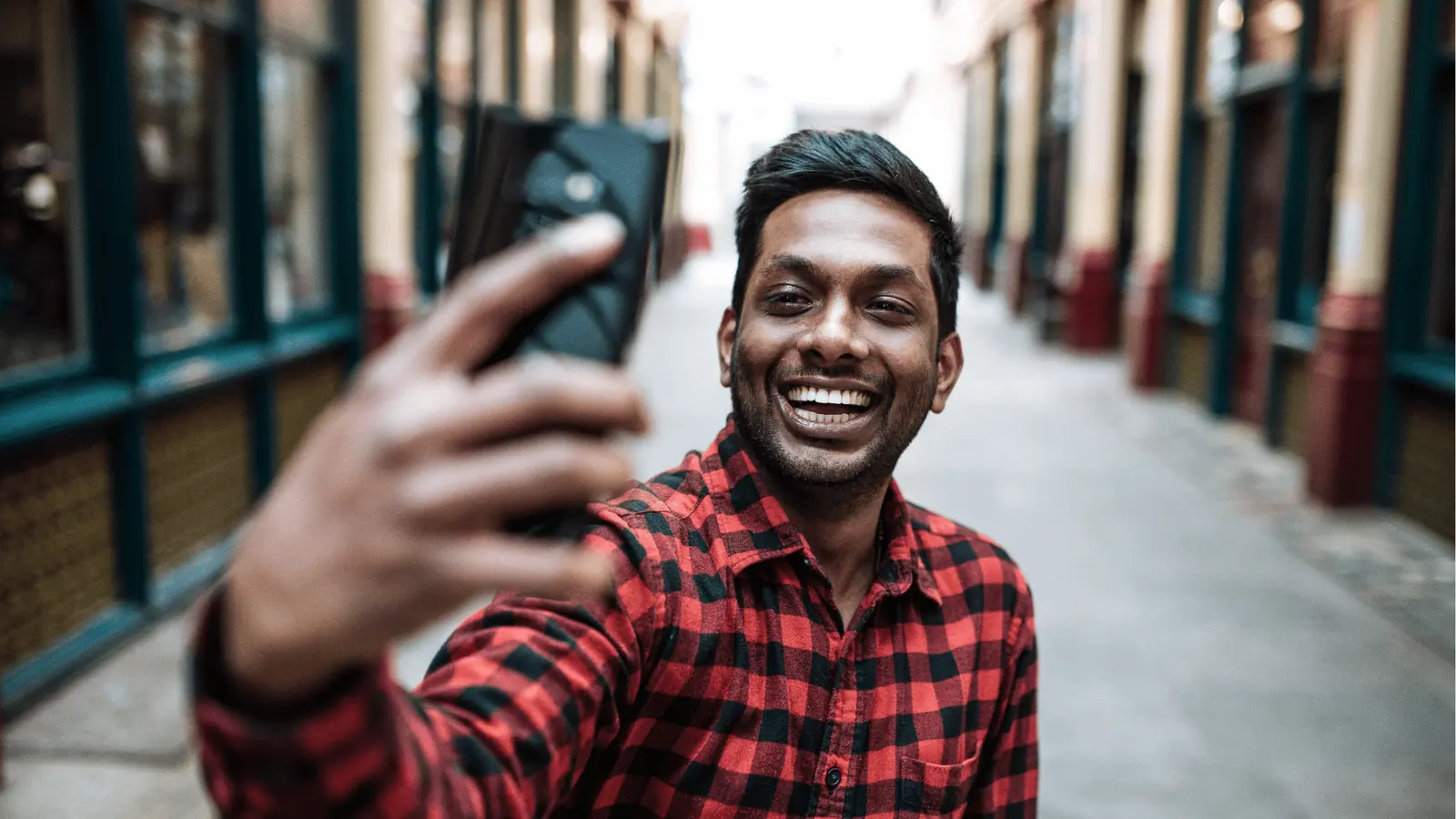 Smiling man in red plaid shirt taking a selfie with smartphone