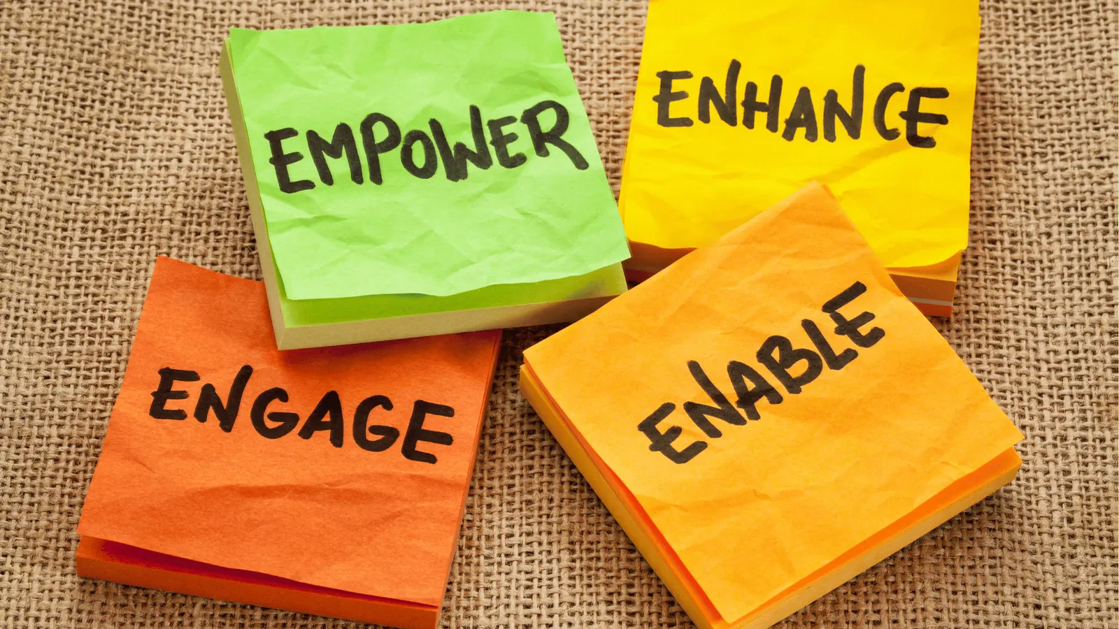 Stacked colored sticky notes reading empower engage enhance enable on burlap