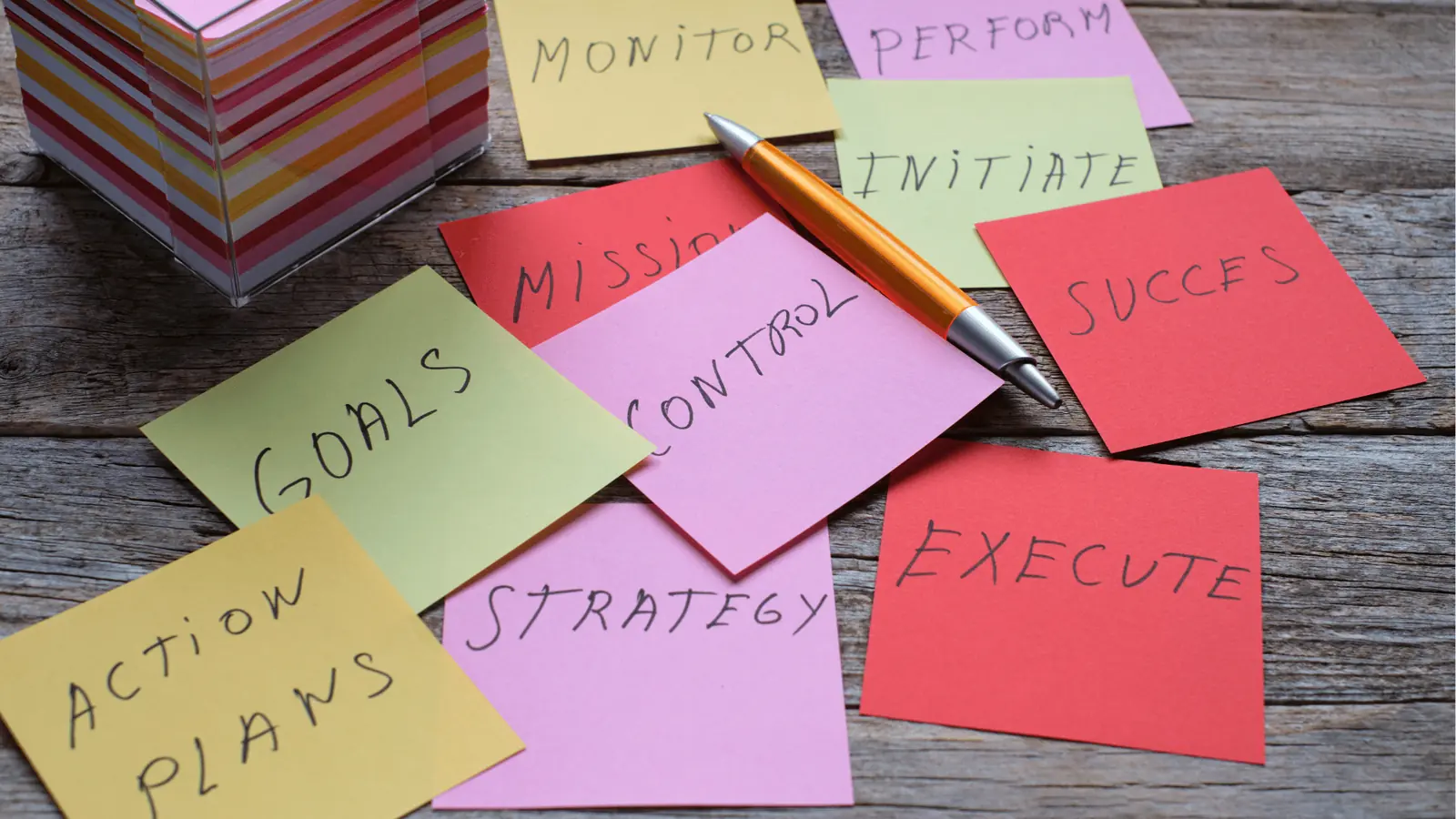 Colorful sticky notes with handwritten planning words and an orange pen on wood