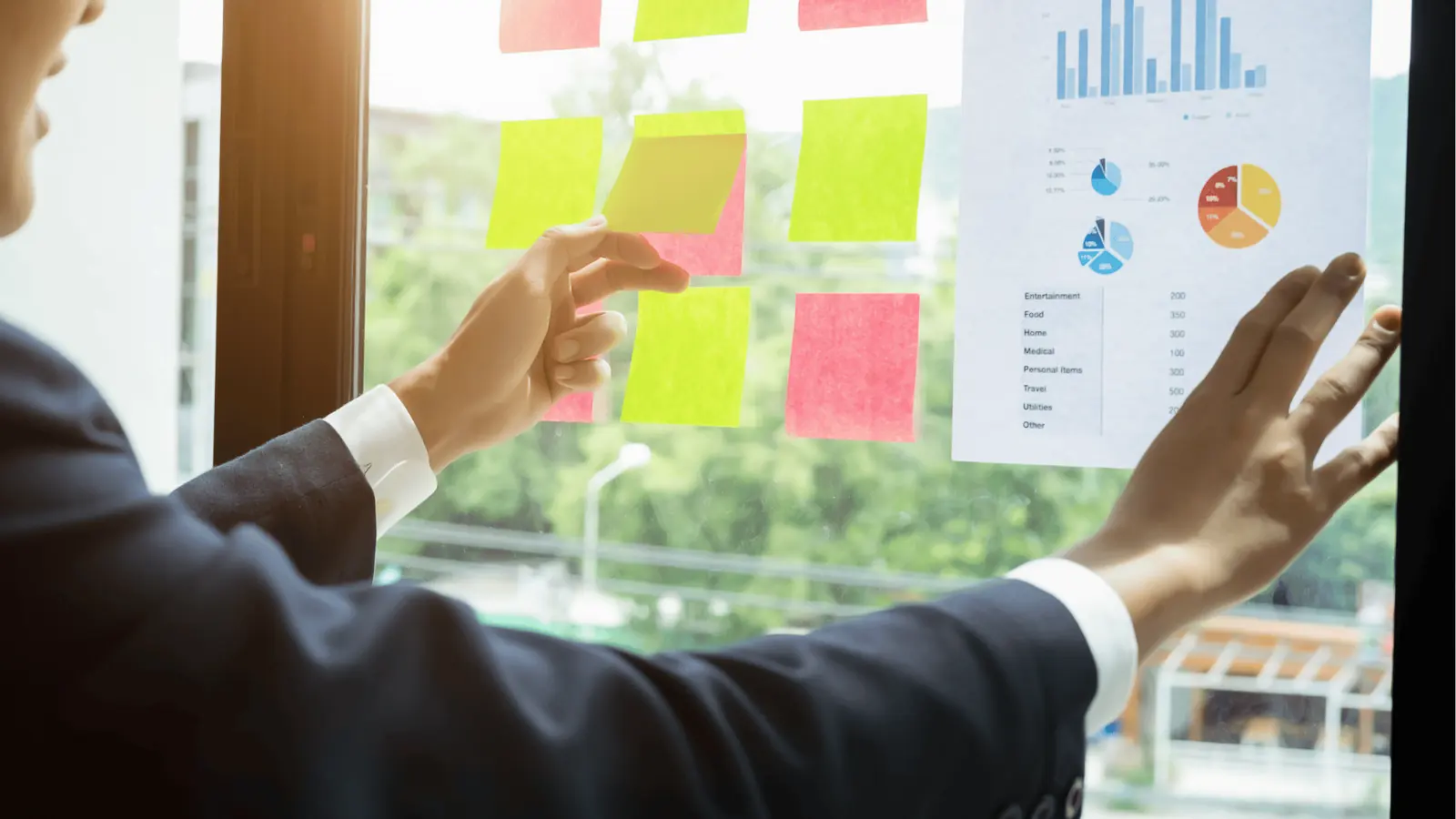 Person placing pink and yellow sticky notes on window next to printed chart