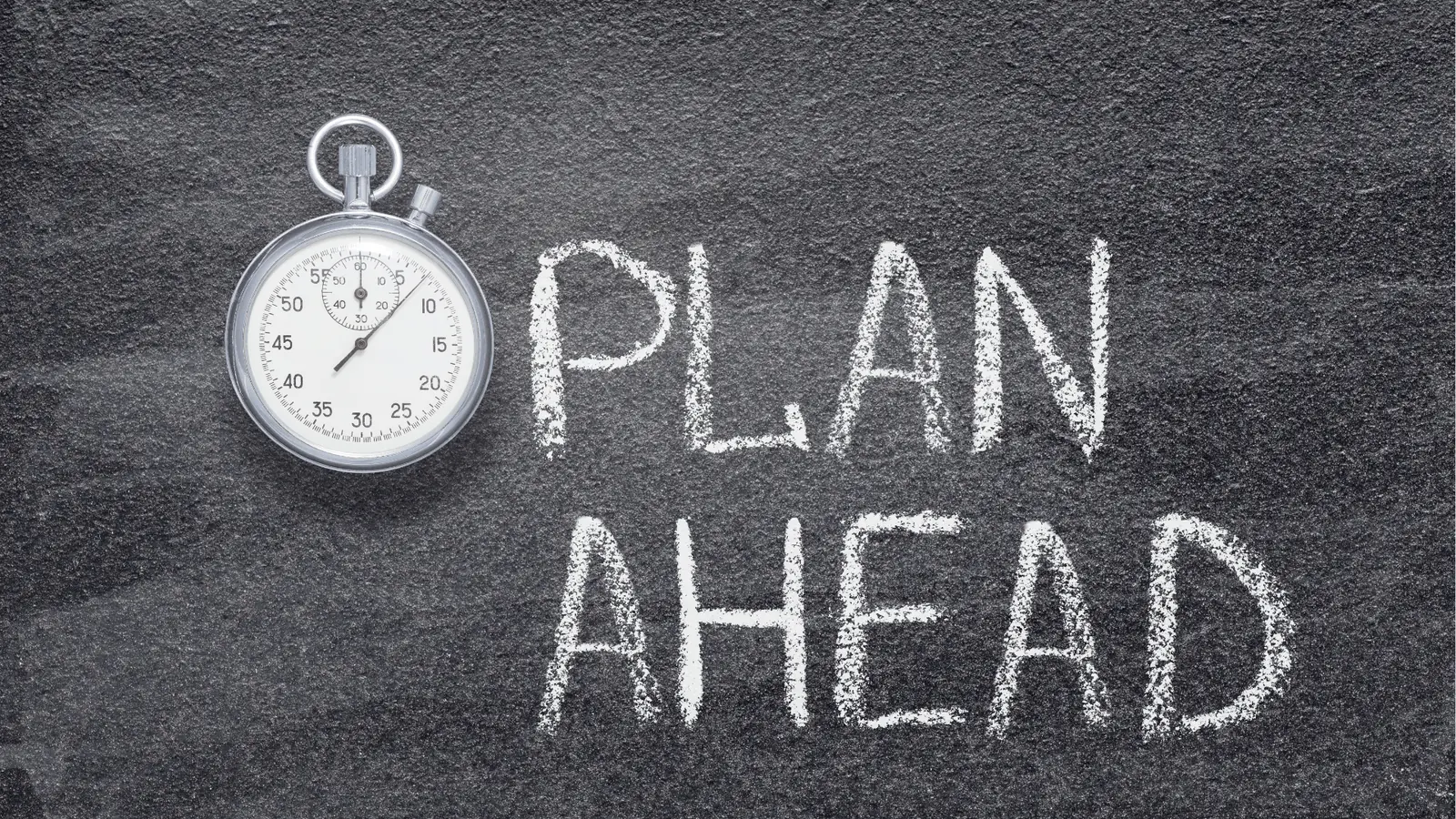 Silver stopwatch on chalkboard next to the words PLAN AHEAD written in chalk