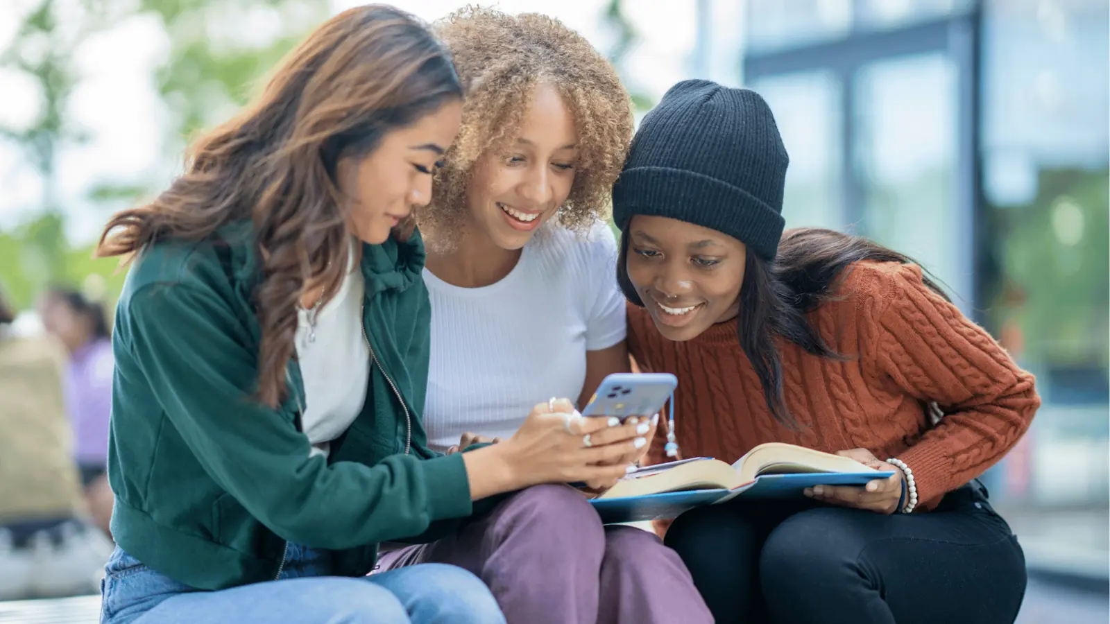 Three young women on a bench looking at a smartphone and smiling