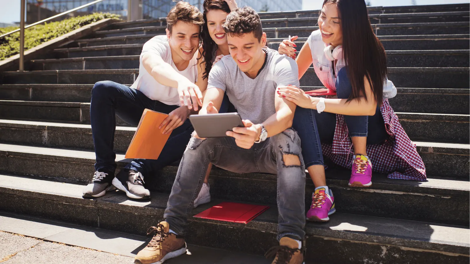 Four young people sitting on outdoor steps looking at a tablet together