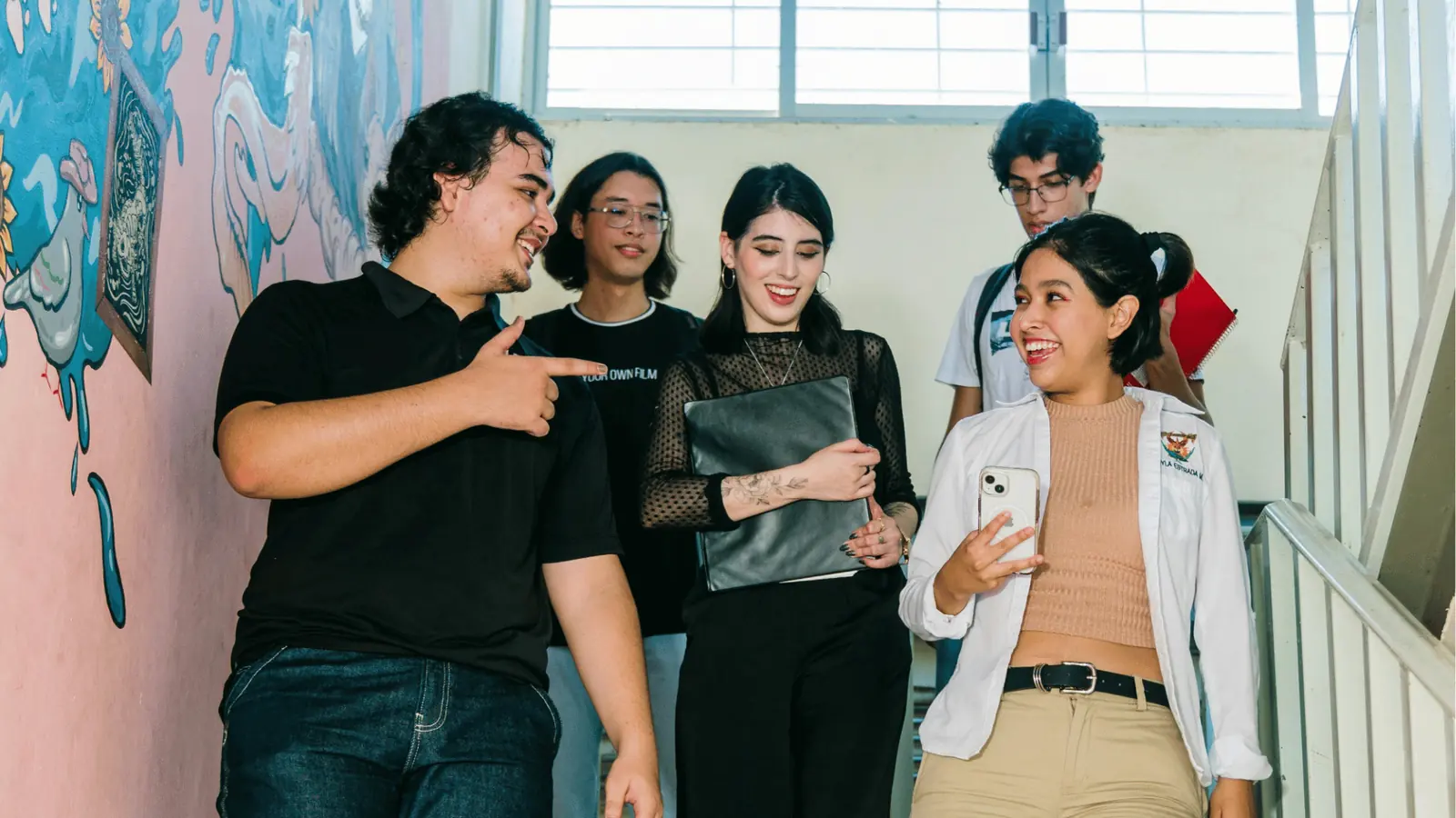 Five students walking down a stairwell laughing and looking at a phone