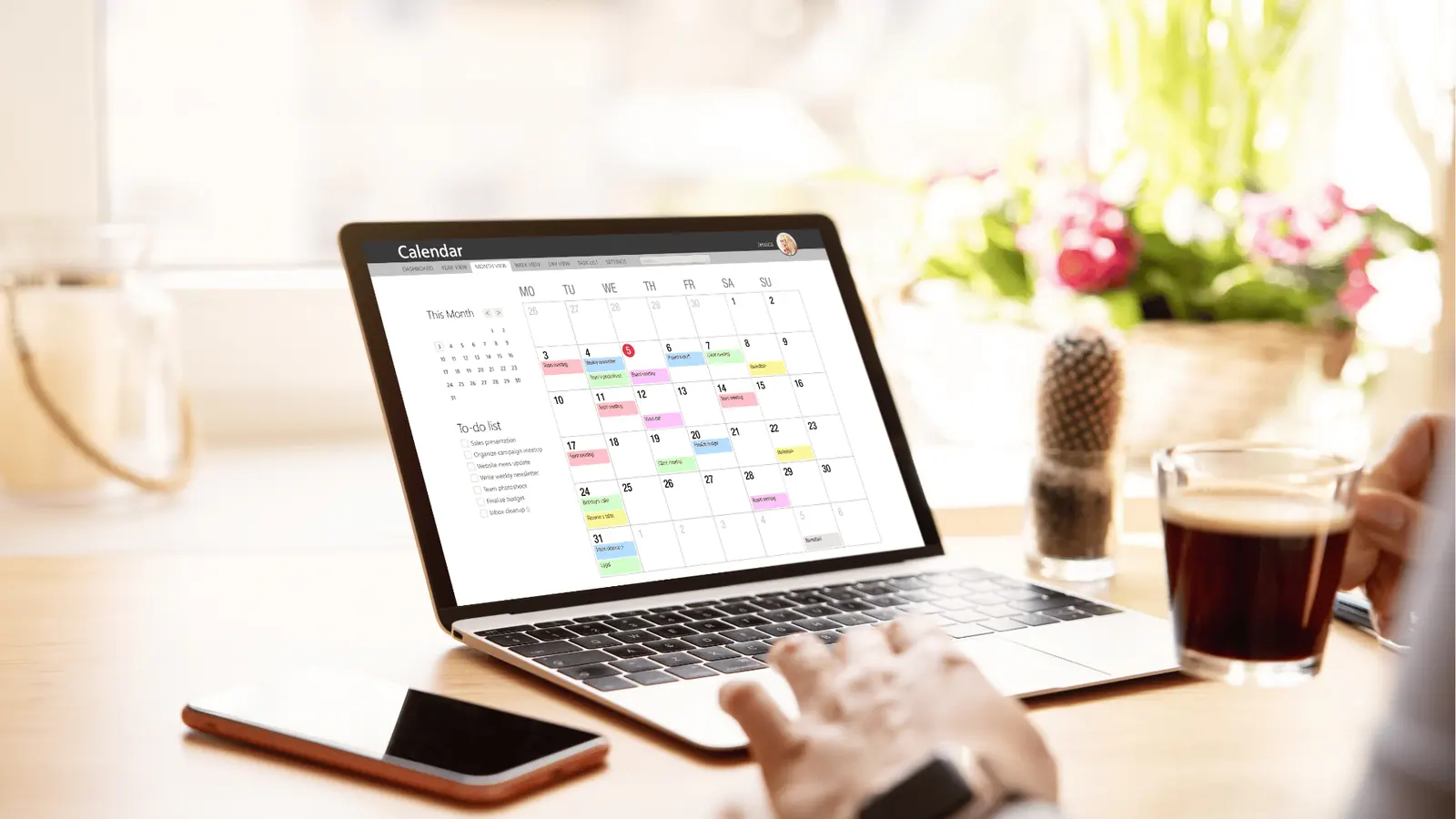 Hands using a laptop displaying a monthly calendar app while holding a cup of coffee for automation