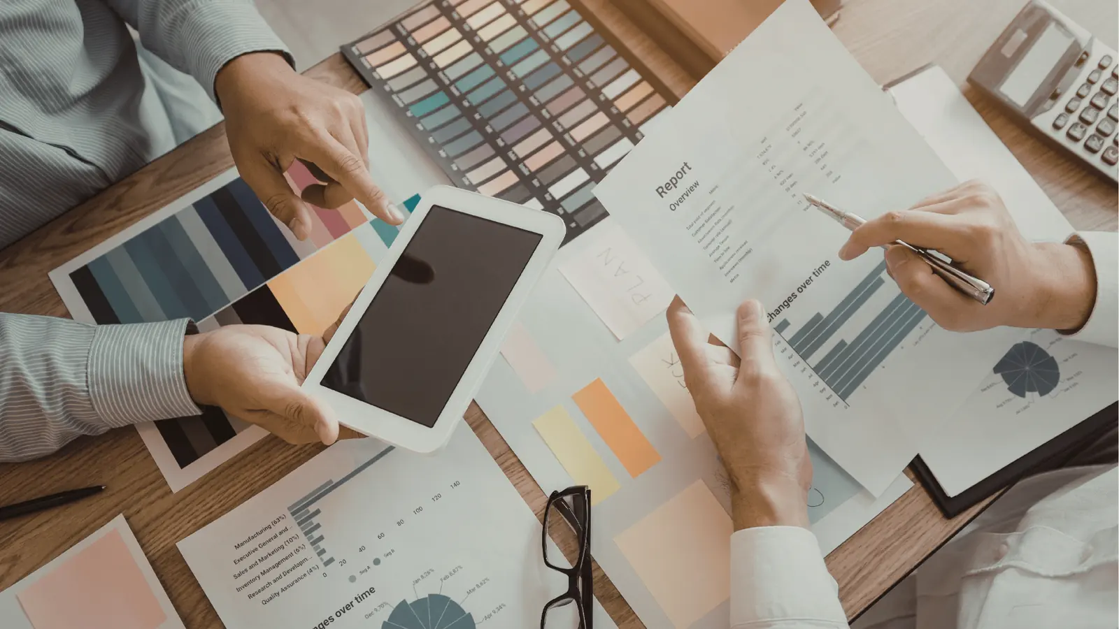 Two people reviewing color swatches, charts, and a tablet at wooden desk