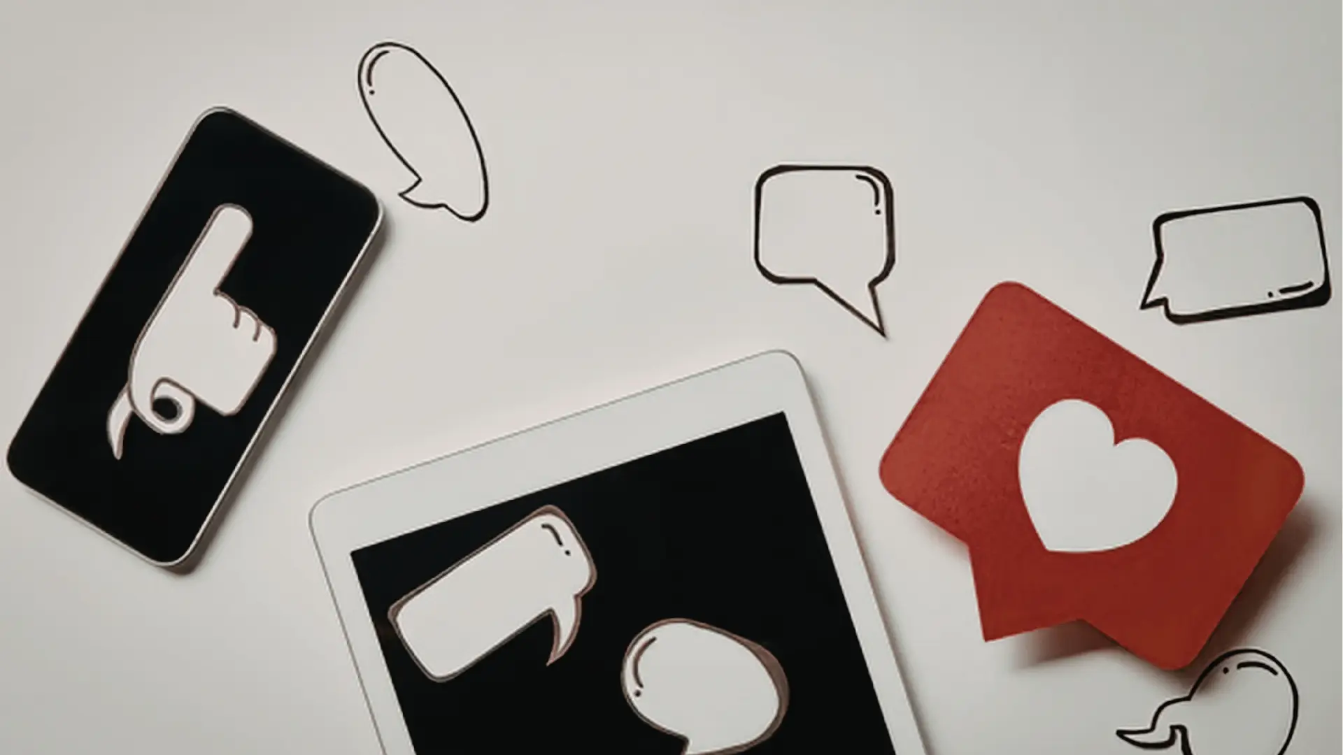 Overhead view of smartphone, tablet and paper chat bubbles with heart and thumbs-up