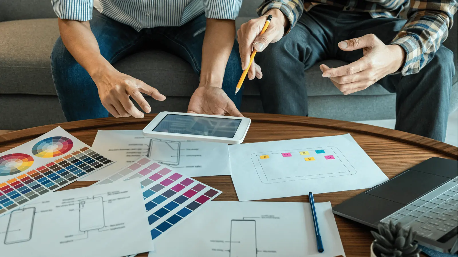 Two people reviewing tablet and printed wireframes on table with color swatches for AI-assisted workflow