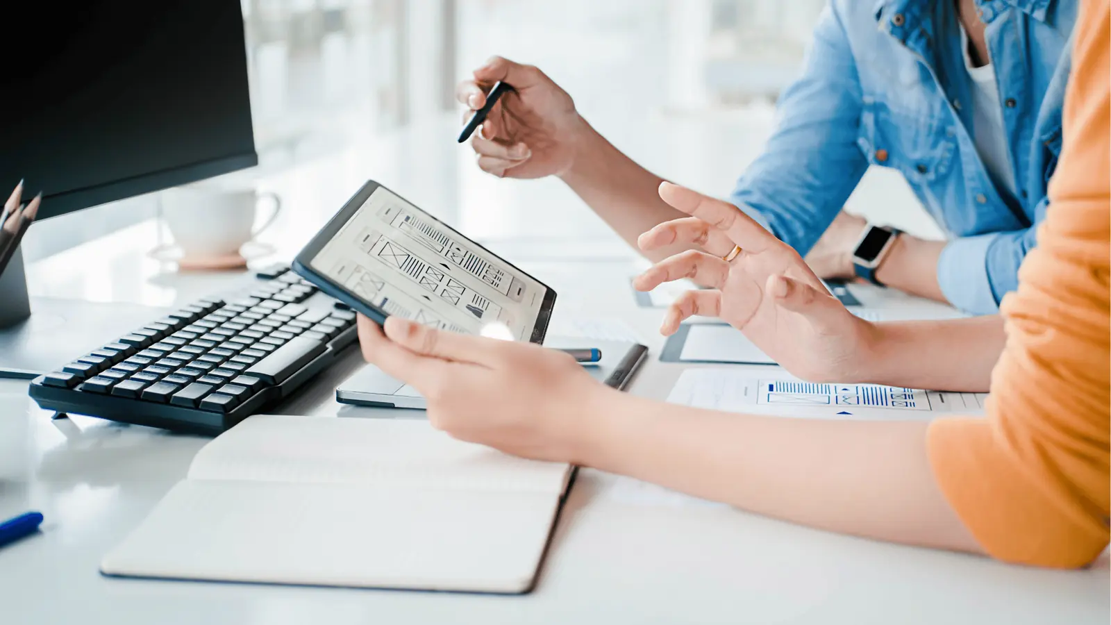 Two people reviewing app wireframes on a tablet at a bright desk