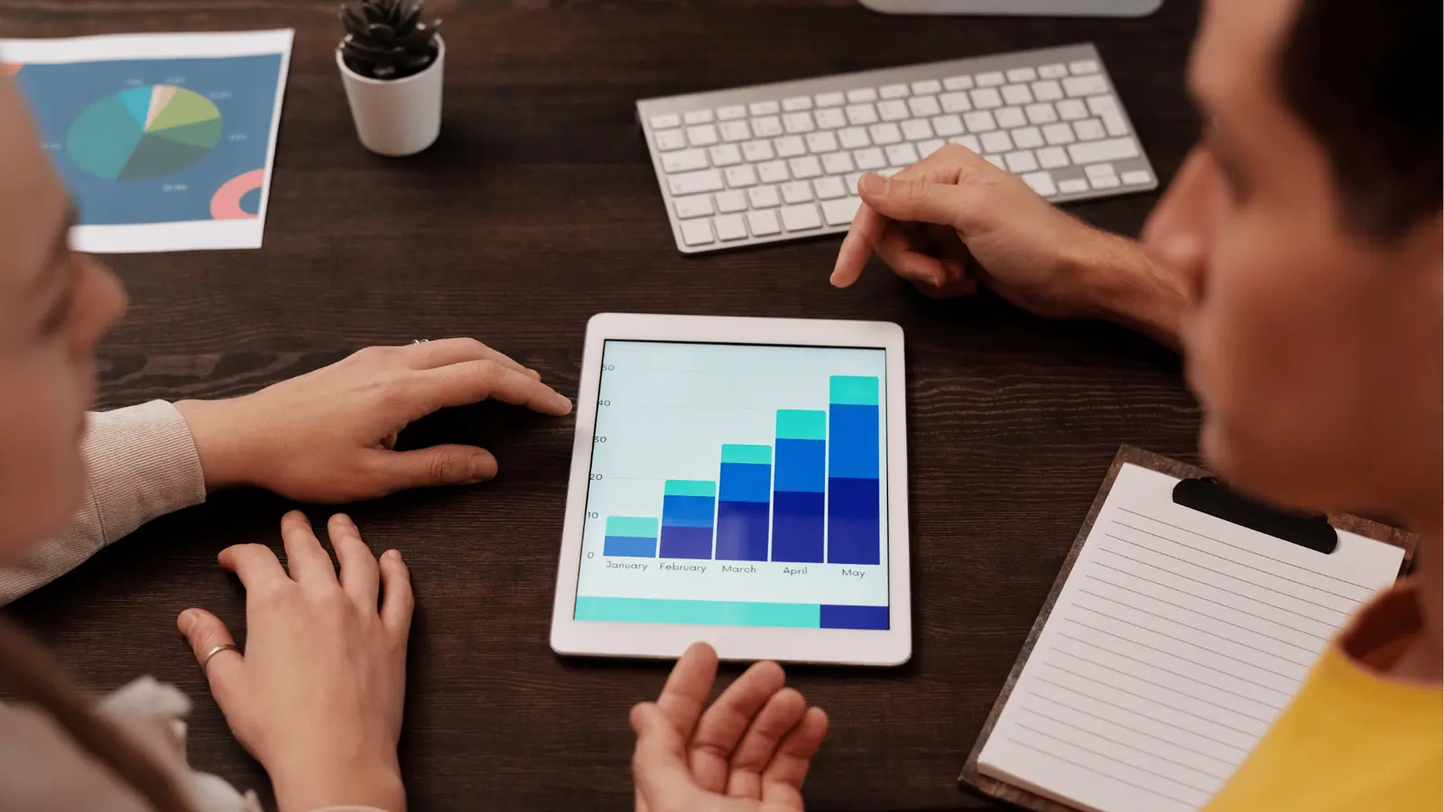 Hands around tablet displaying rising stacked bar chart from January to May