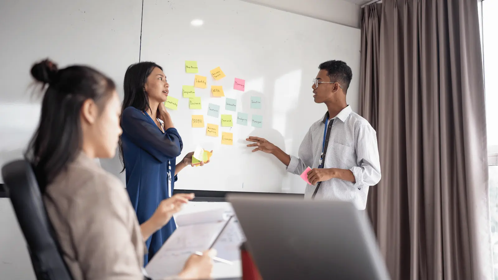 Three coworkers discussing sticky notes on a whiteboard during a meeting
