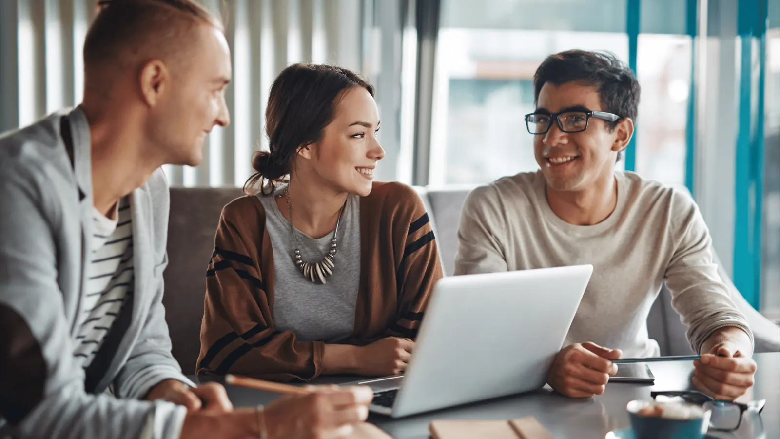 Three young colleagues smiling and talking around a laptop in meeting