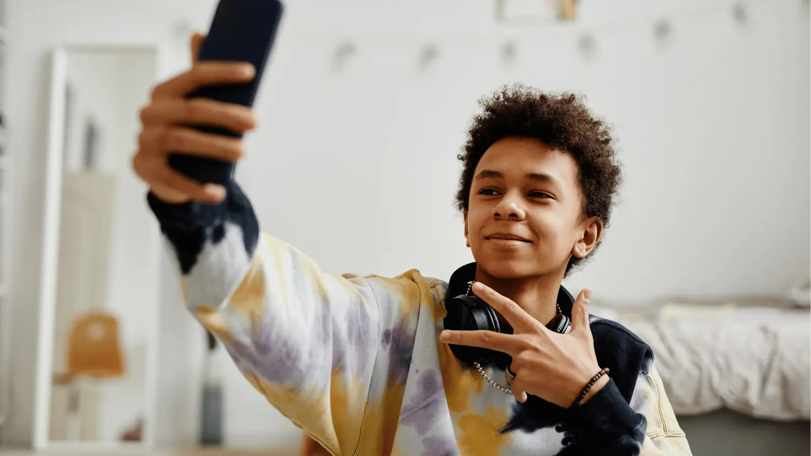 Teenager taking a selfie with headphones around his neck in bedroom