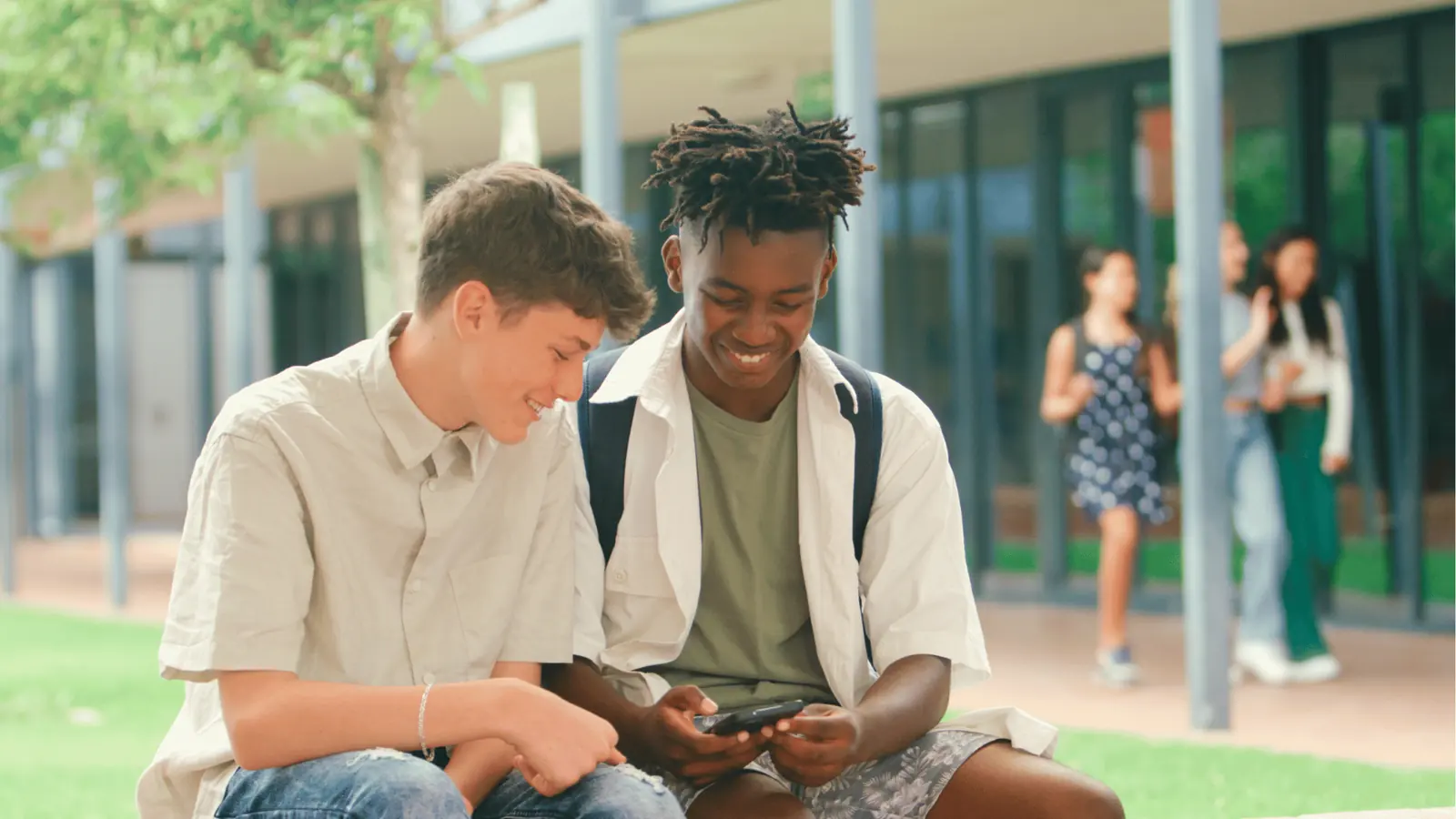 Two teenage boys sitting outdoors at school looking at a smartphone together