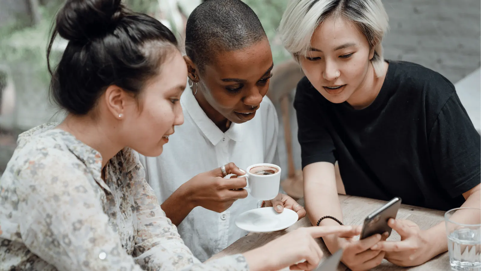 Three people at a table looking at a smartphone while sharing coffee