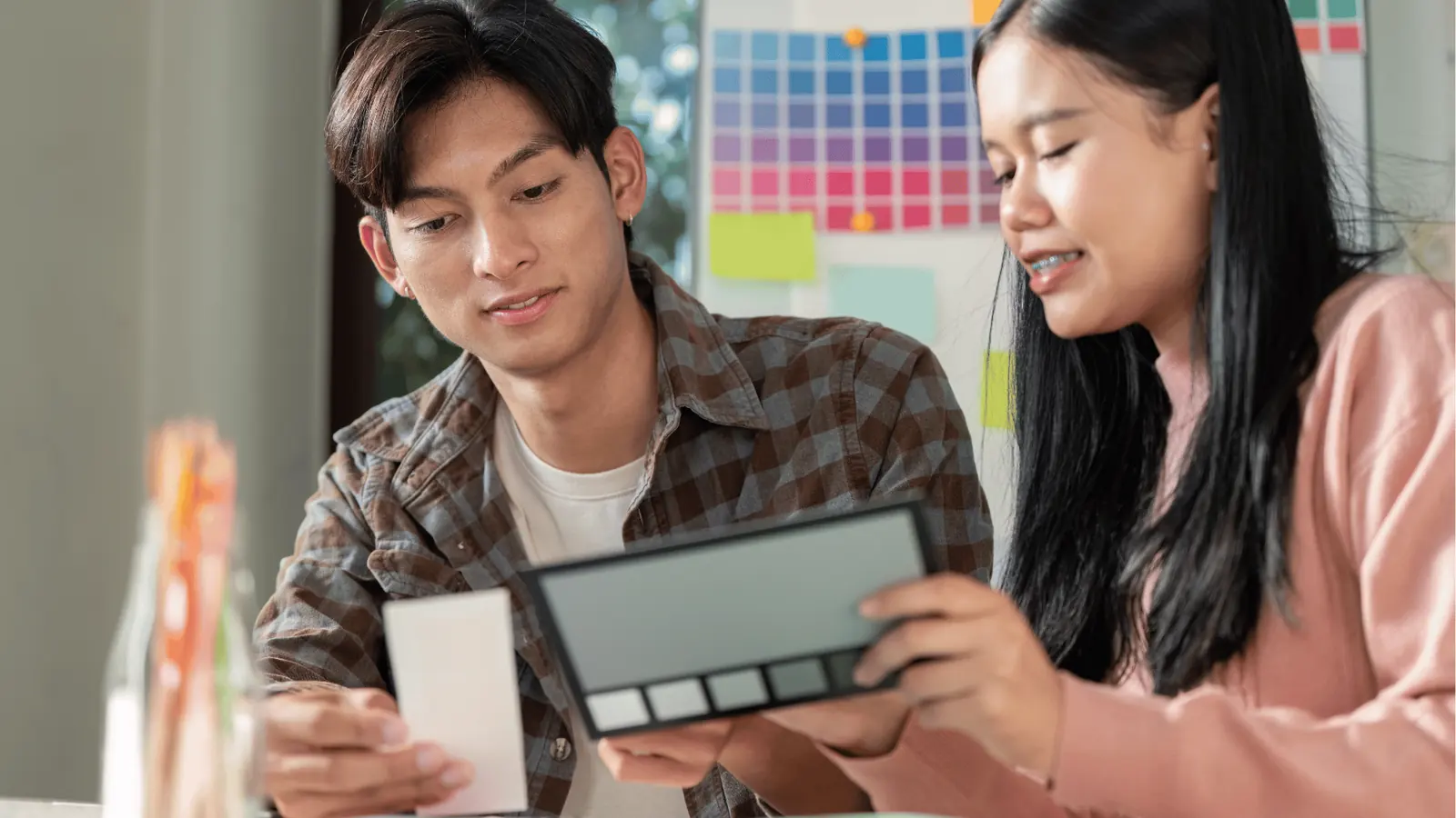 Two people comparing color swatches and a palette in a bright workspace for creative production