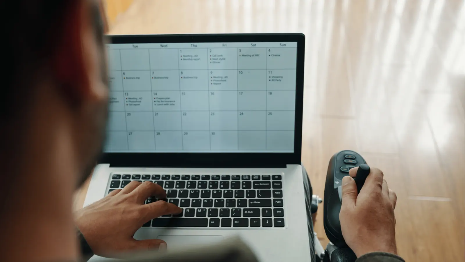Person in wheelchair using laptop showing a monthly calendar on screen