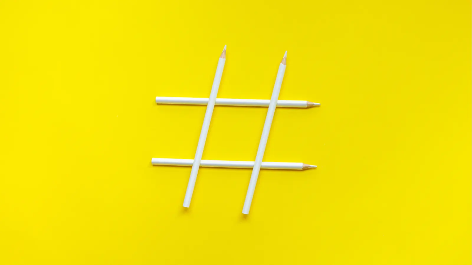 White pencils arranged into a hashtag symbol on a yellow background