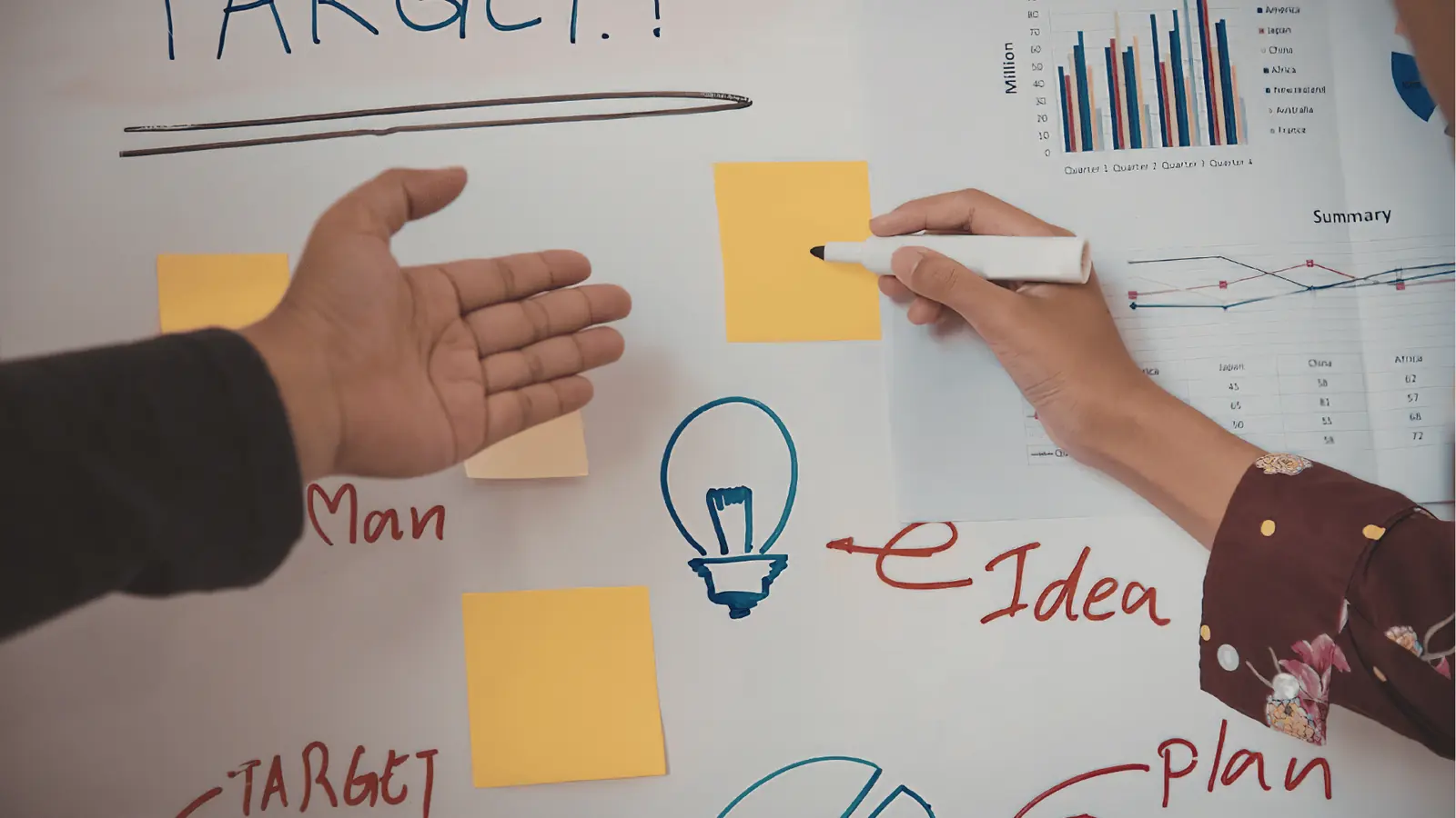 Two hands arranging sticky notes and drawings on a whiteboard for scheduling
