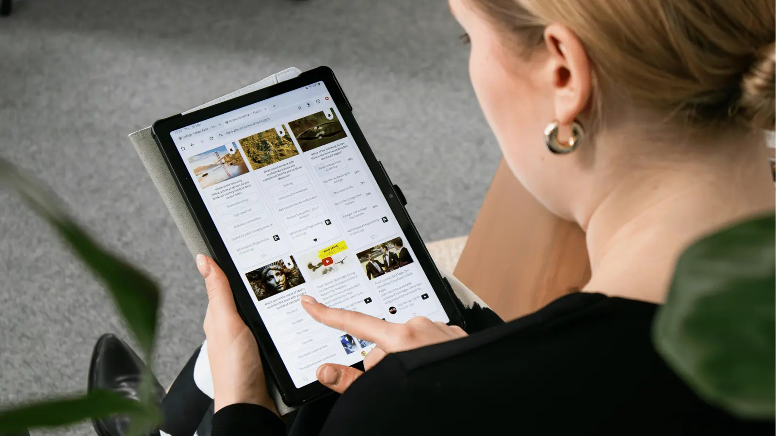 Woman sitting and tapping a tablet showing article thumbnails grid