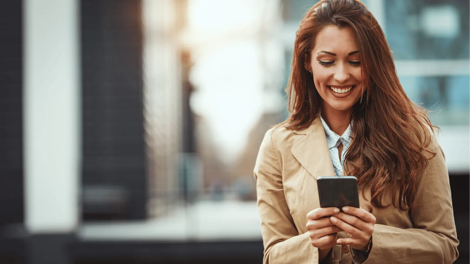 Smiling woman outdoors looking at smartphone while standing on city street