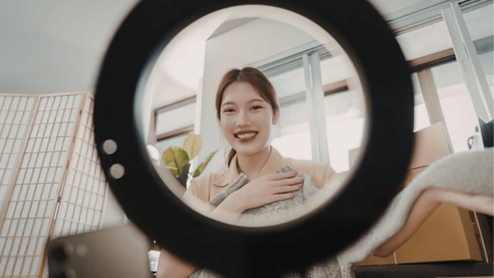 Young woman smiling at camera through ring light while holding a blanket for community management
