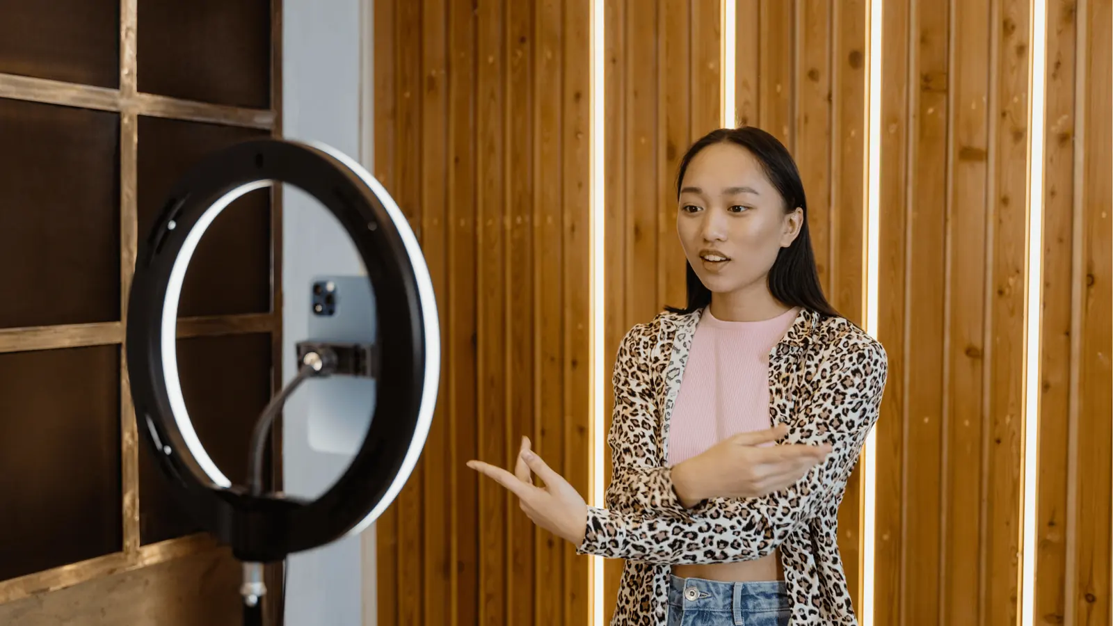 Young woman speaking to camera with ring light in wooden studio for team collaboration