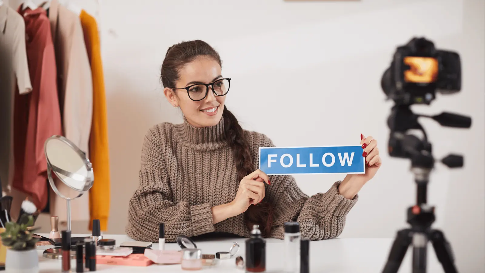 Smiling woman vlogger holds blue FOLLOW sign in front of camera