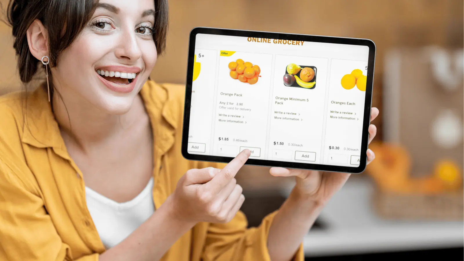 Smiling woman points to tablet showing an online grocery page with oranges