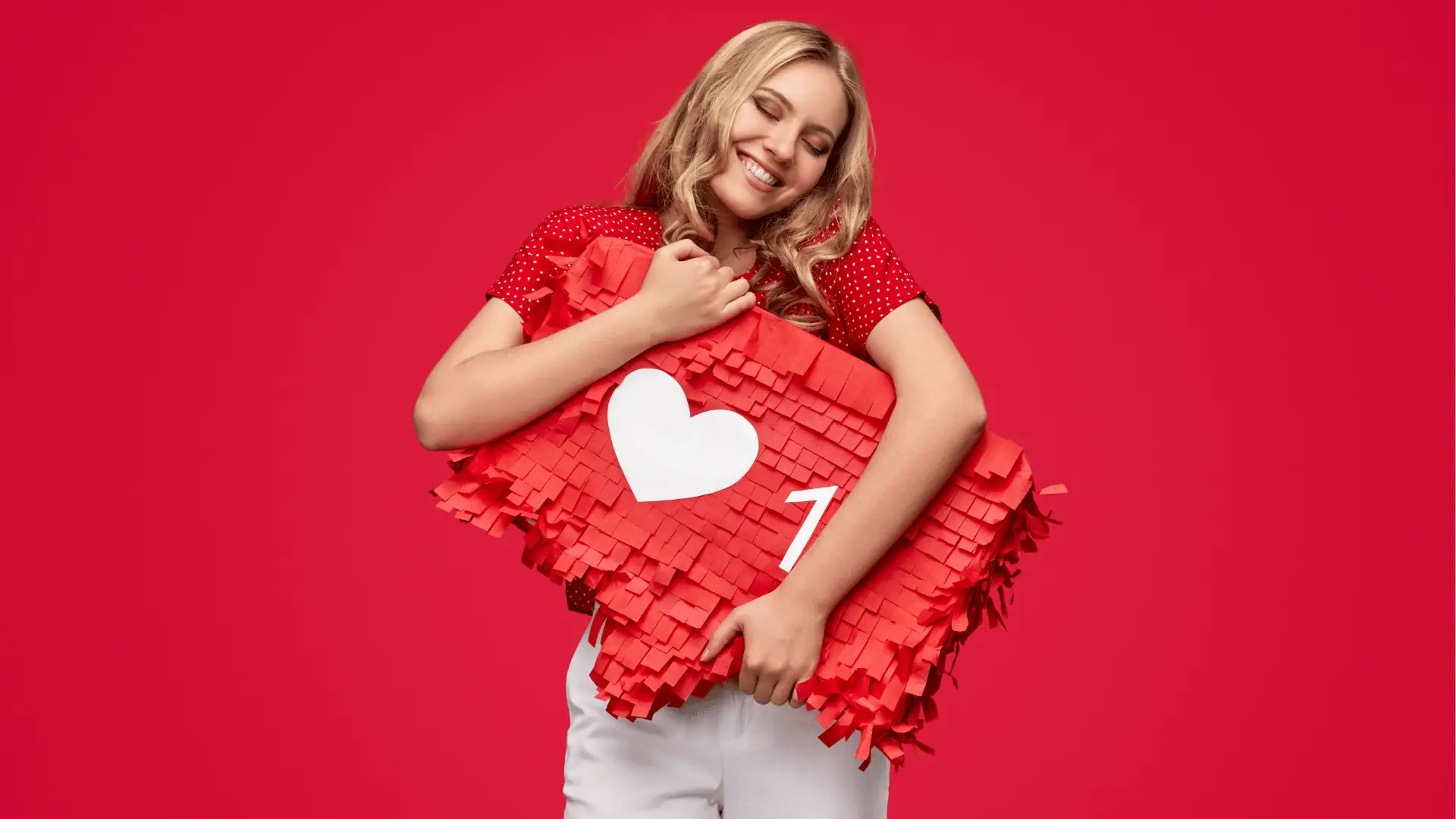 Smiling woman hugging a red heart-shaped pinata against red background