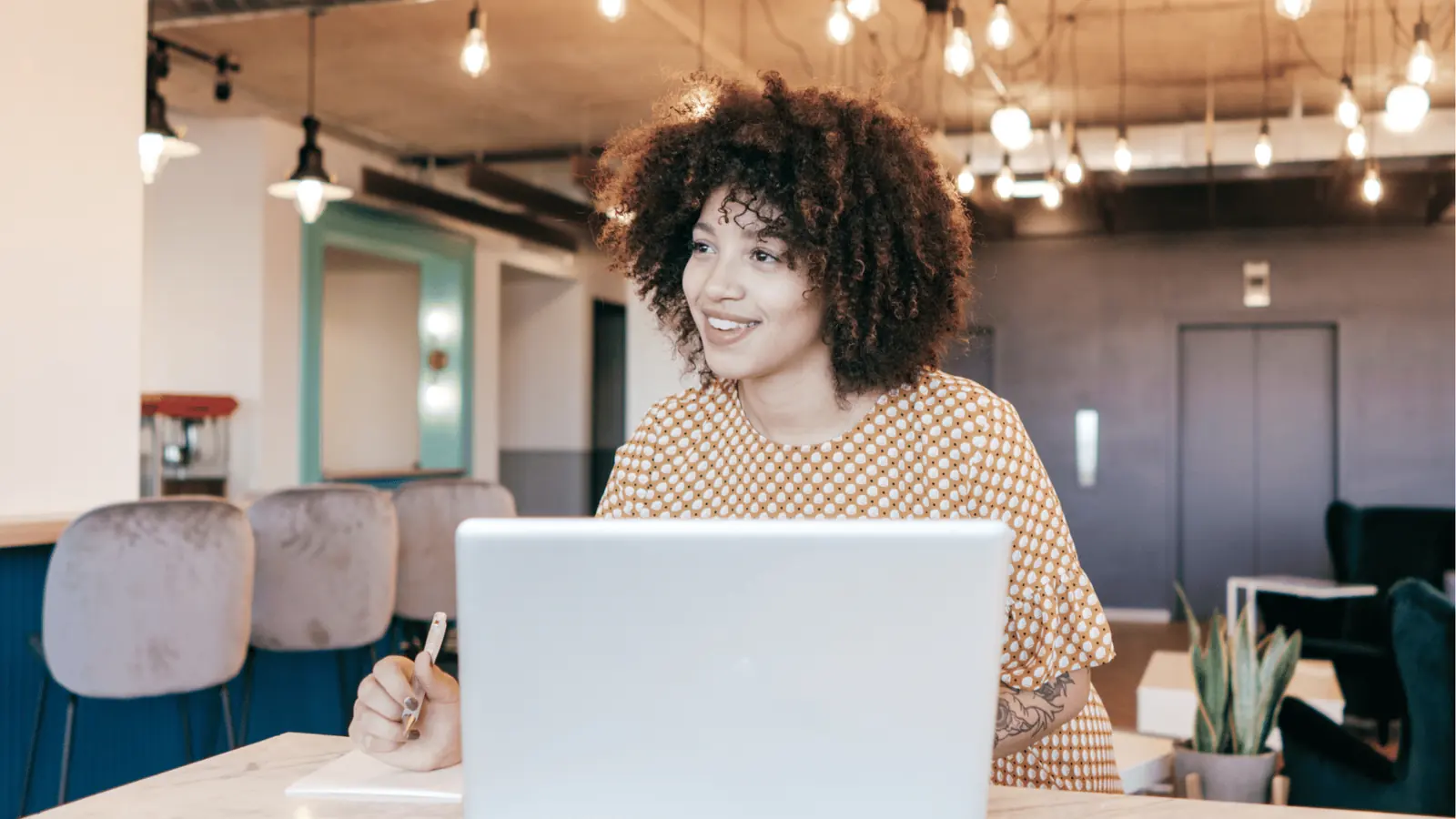 Young woman smiling at laptop in modern coworking space holding a pen