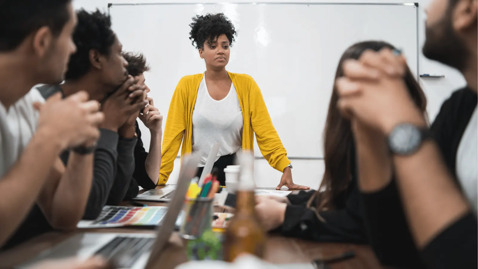 Woman in yellow cardigan leading a team meeting at conference table