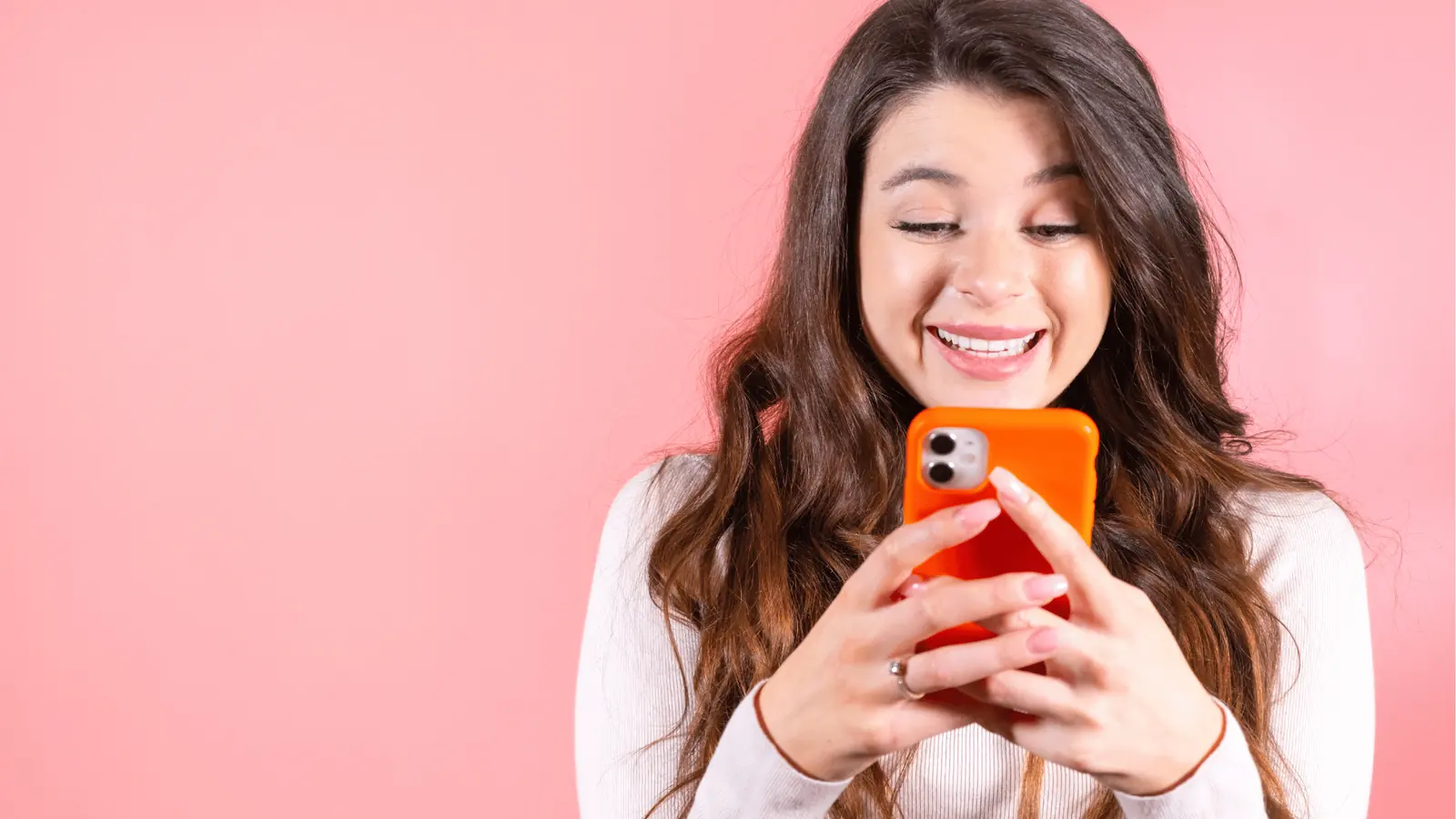 Young woman smiling while looking at orange phone against pink background