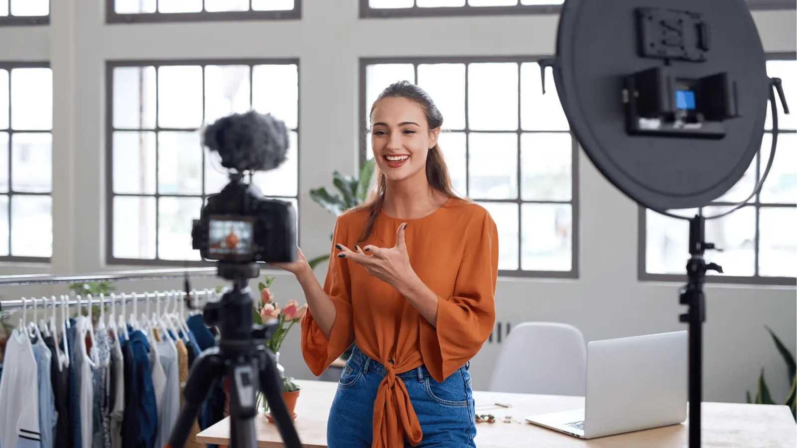 Smiling woman recording a fashion video with camera, ring light, and laptop for creative production