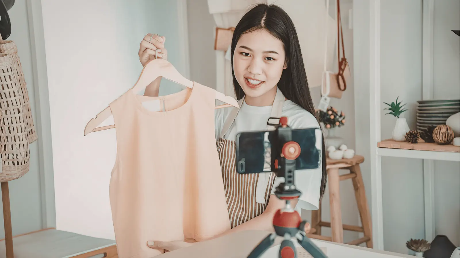 Young woman holding a peach dress on a hanger in front of smartphone camera for approval workflow