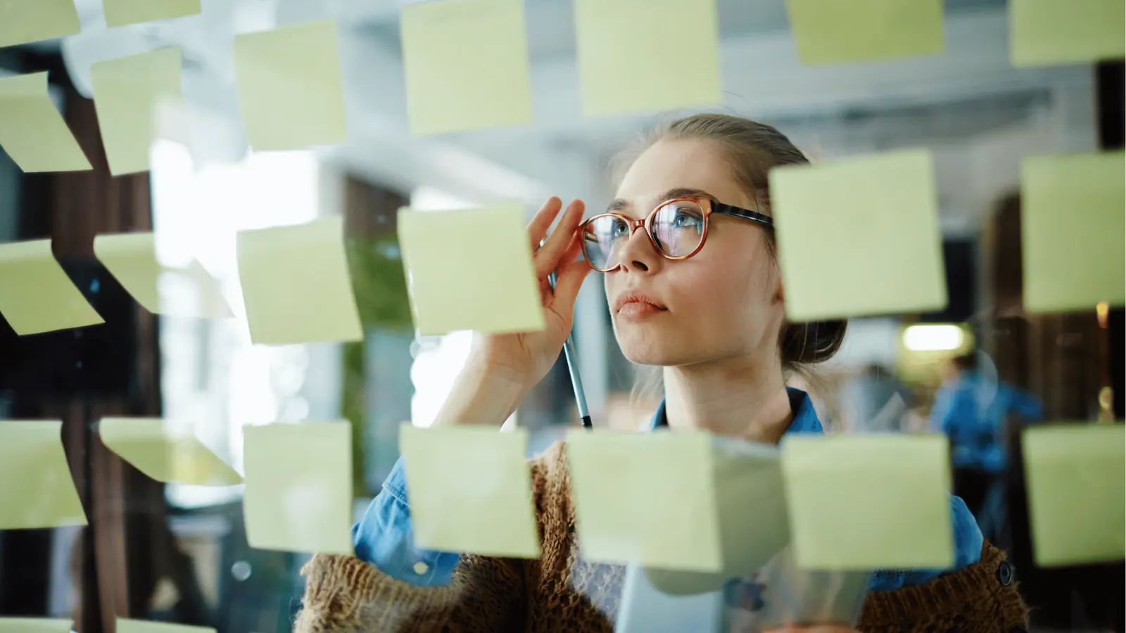 Young woman reviewing yellow sticky notes on glass wall in office