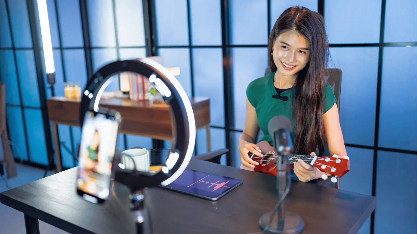 Young woman smiling while playing ukulele in a live-stream setup for workflow