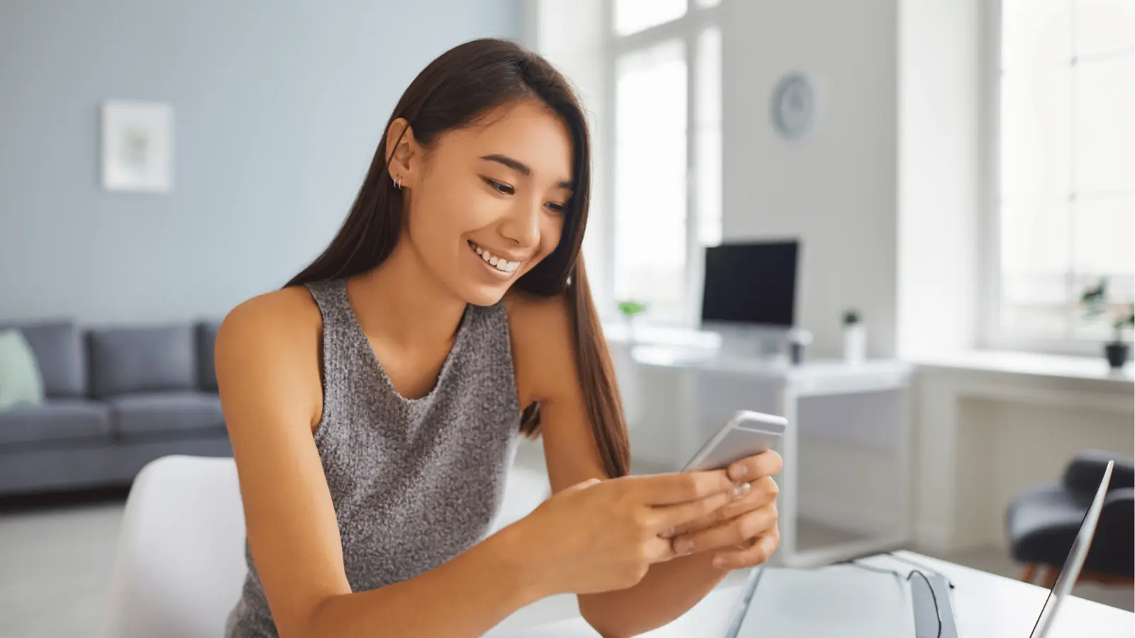 Smiling woman in home office looking at her smartphone while seated