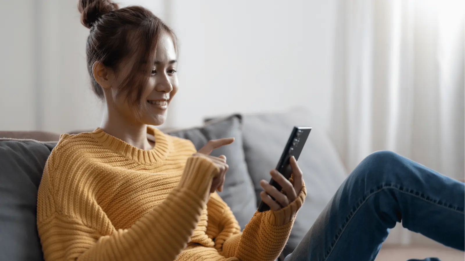 Young woman smiling on couch while using smartphone with relaxed posture