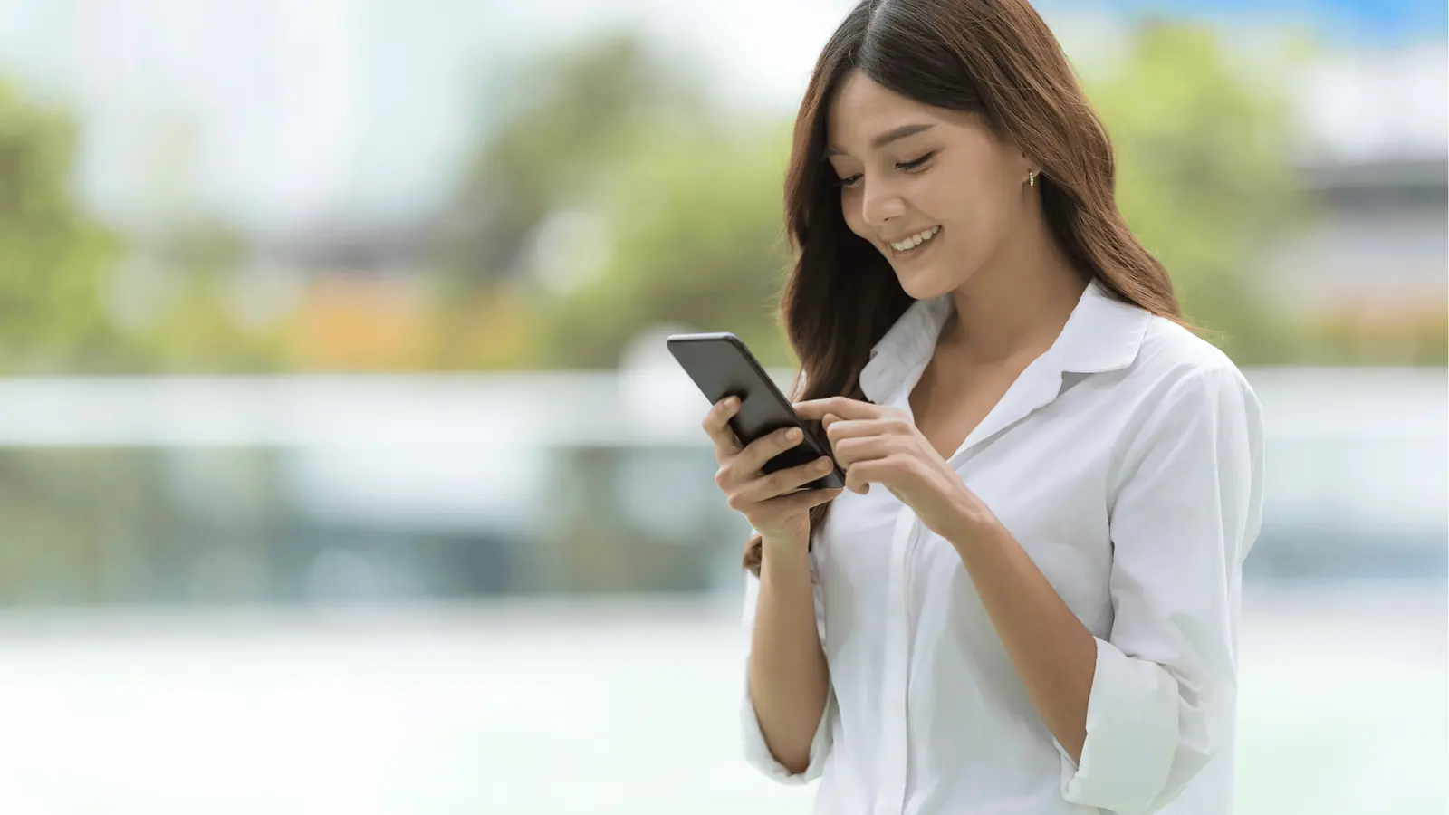 Young woman smiling while using a smartphone outdoors with blurred background