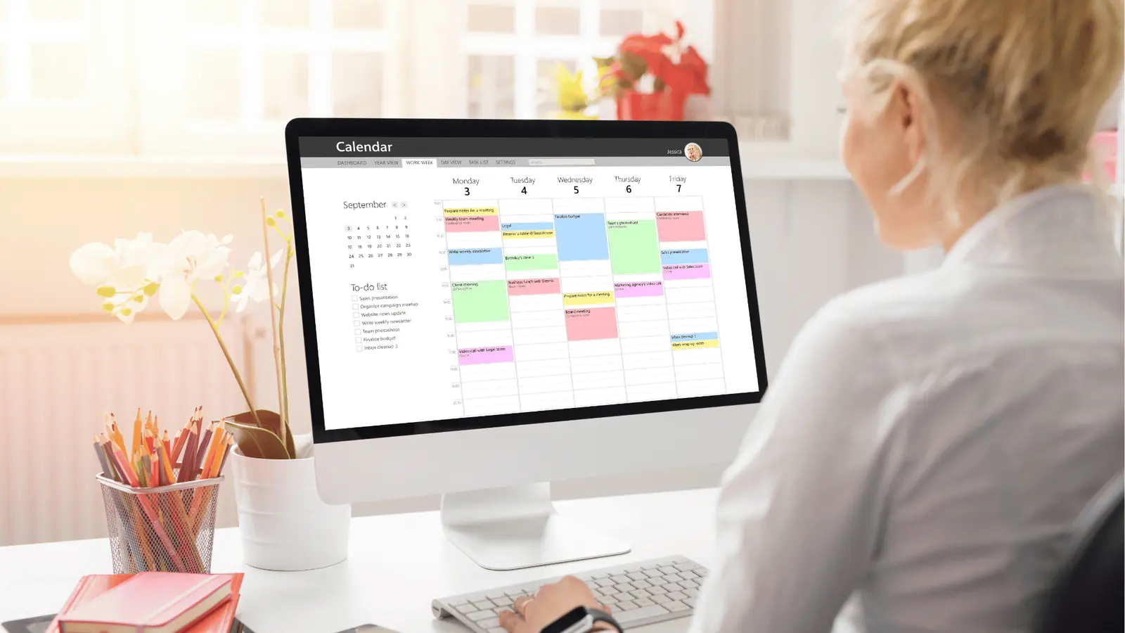 Woman at desk viewing a weekly calendar and to-do list on monitor for AI-assisted workflow