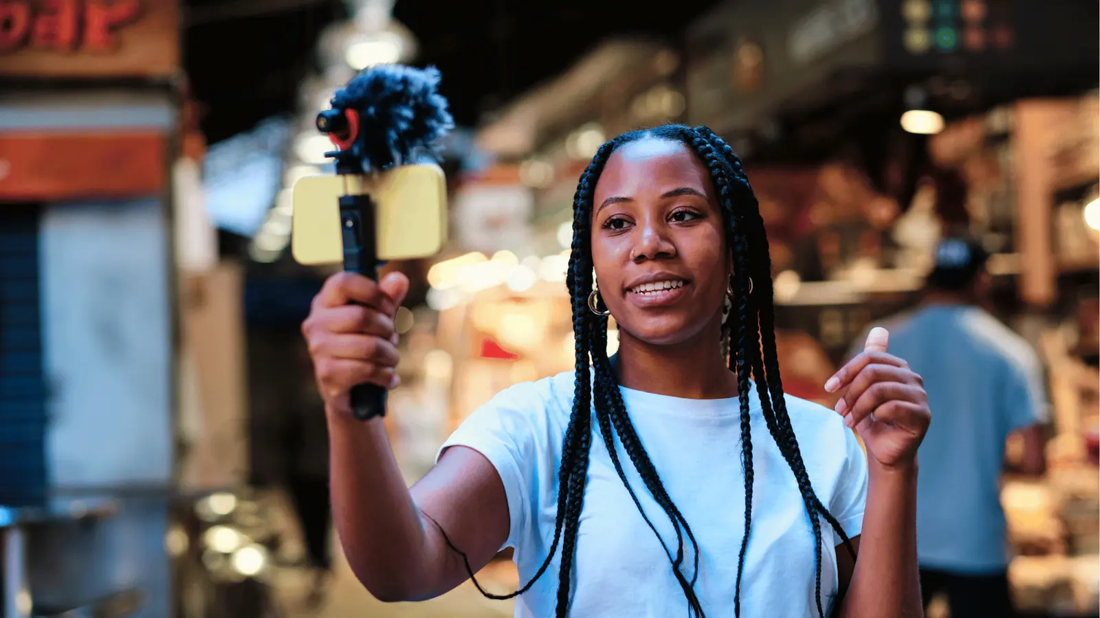 Young woman vlogging with smartphone on handheld microphone inside a market for creative production