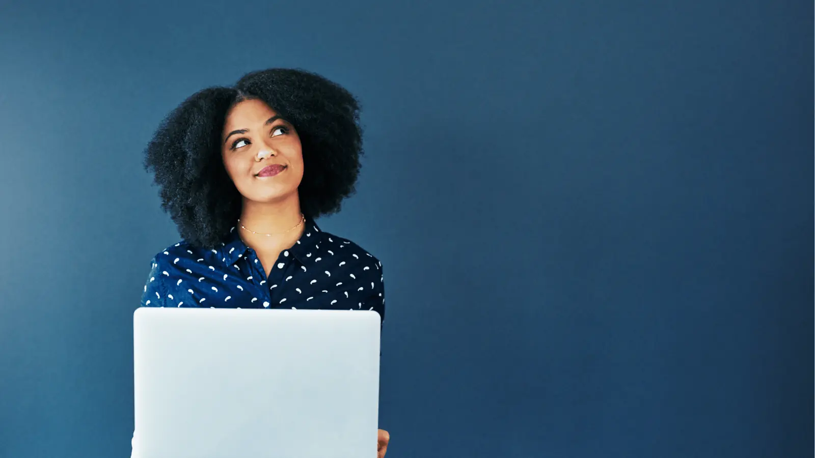 Woman holding laptop and looking up against plain blue background