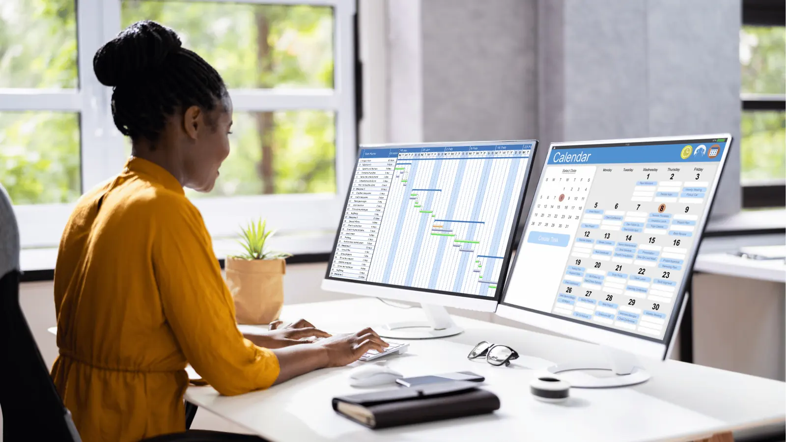 Woman at desk using dual monitors showing calendar and Gantt chart