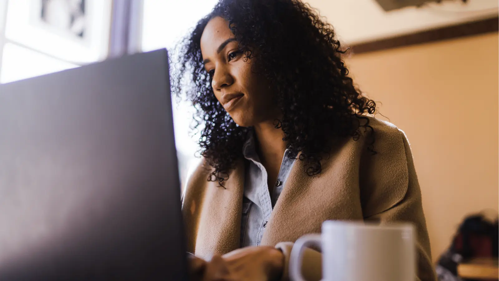 Woman working on a laptop at a table with a coffee mug nearby