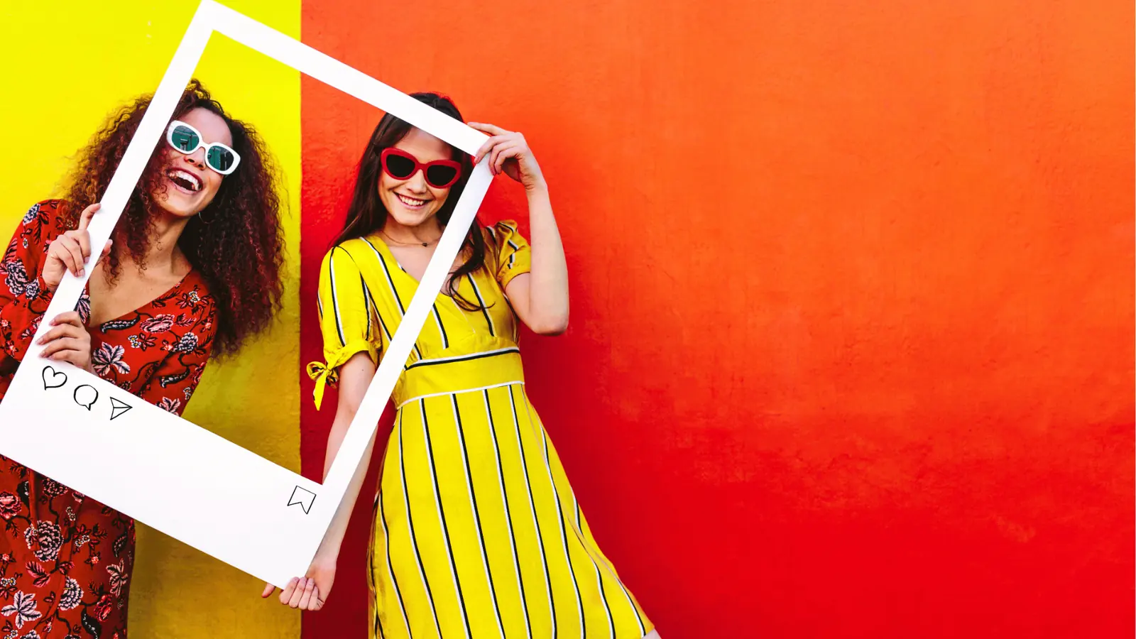 Two smiling women holding a white Instagram-style frame against colorful wall for workflow