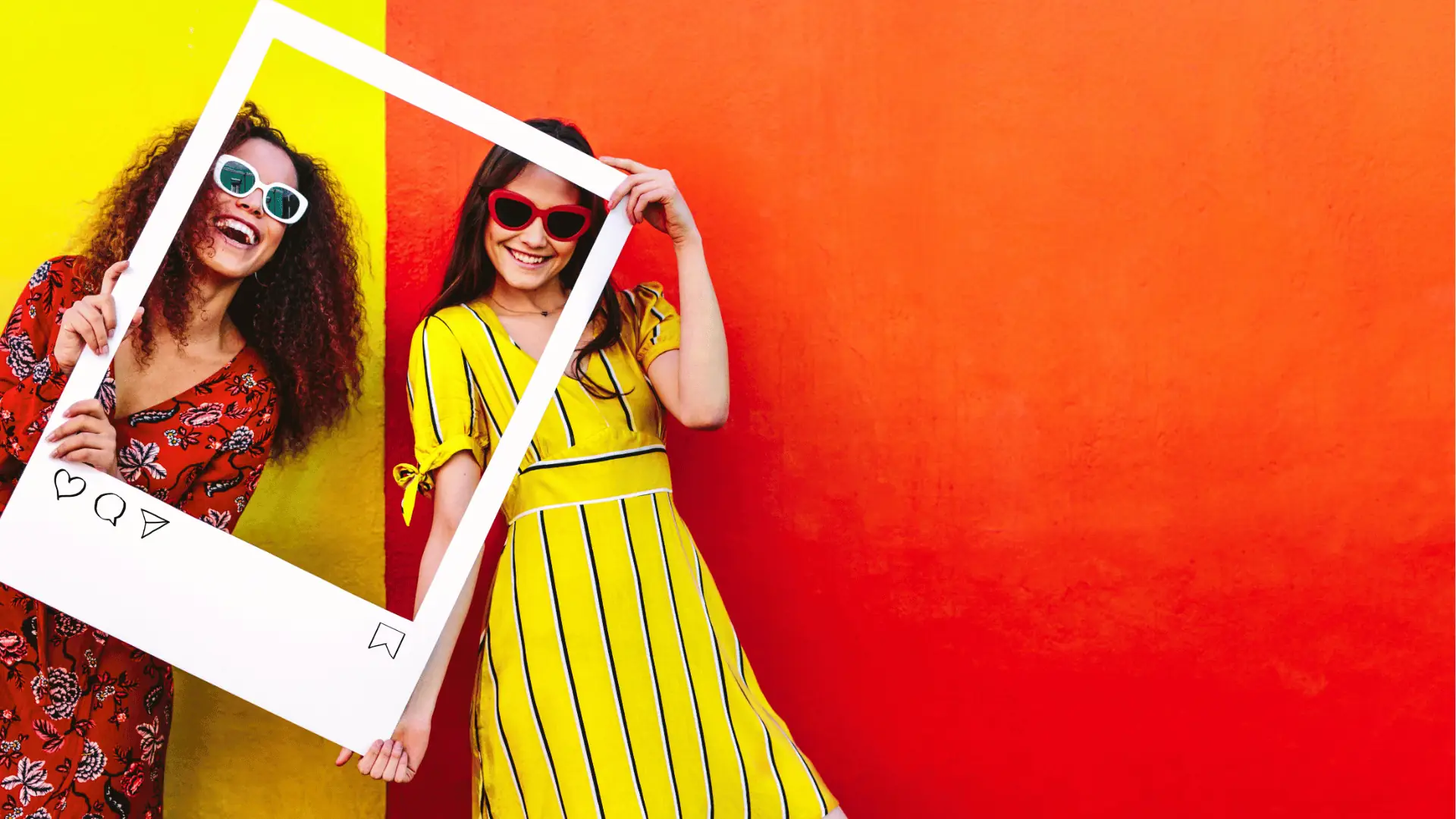 Two smiling women holding an oversized Instagram-style frame against colorful wall