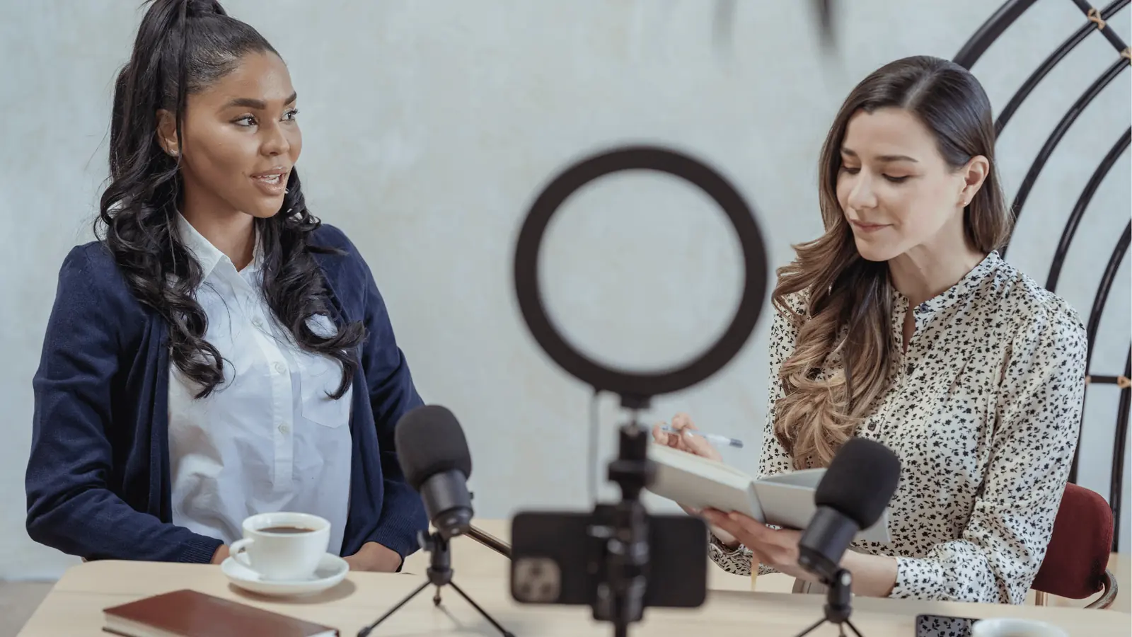 Two women recording a podcast at a table with microphones and ring light for content calendar