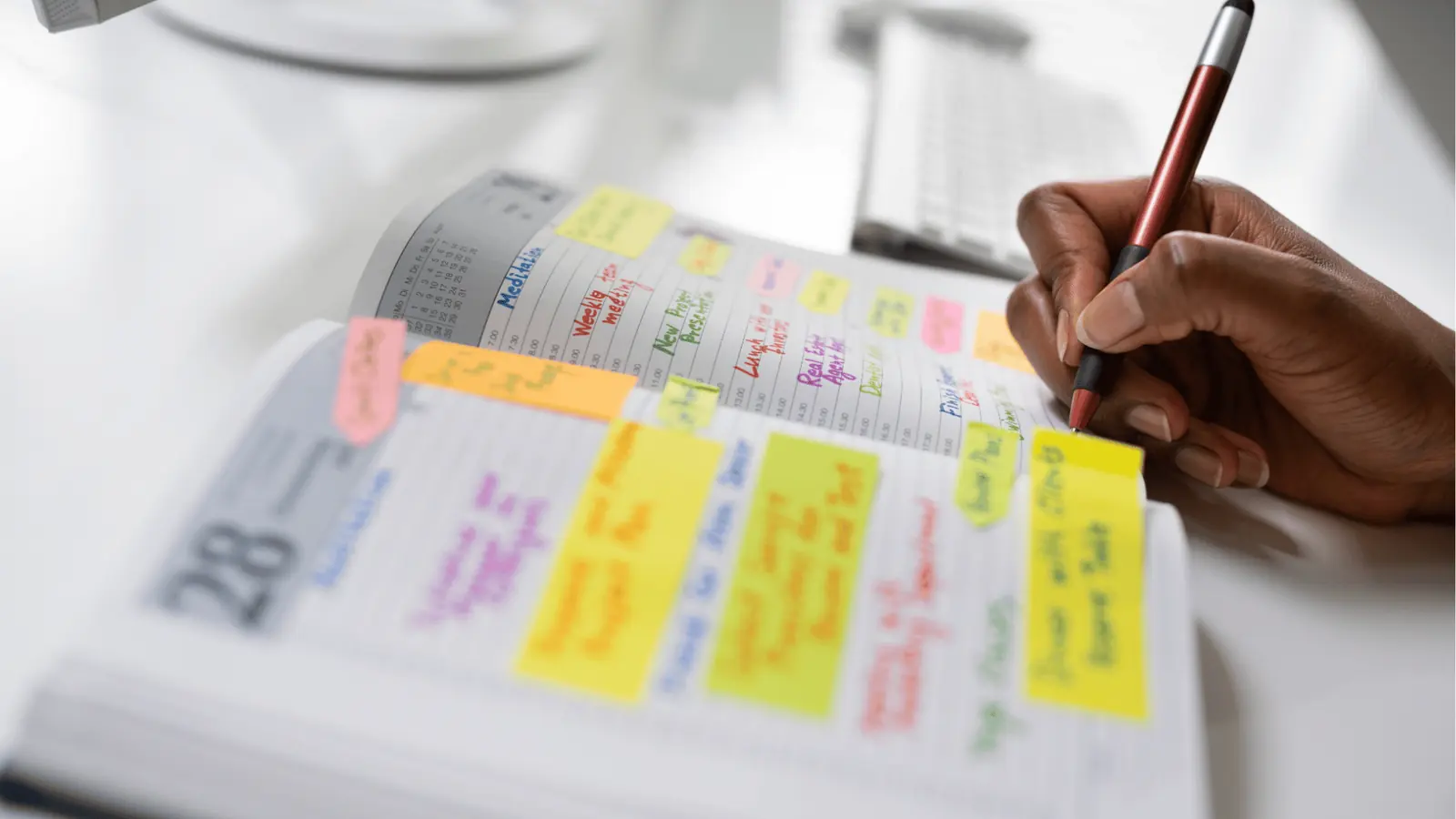 Hand holding a pen writing in a planner full of colorful sticky notes